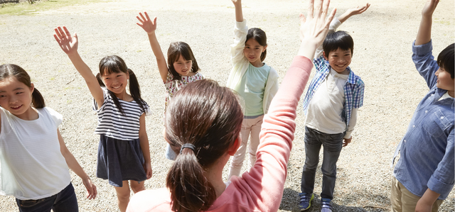 サマーキャンプのスタッフと手を挙げる子供たち